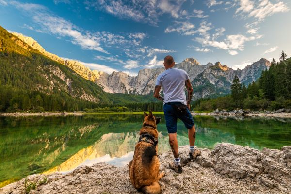 Mensch sitzt mit Hund am Gebirgssee und ist Teil der Natur.
